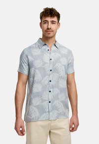 Camisa de manga corta abotonada en tela azul clara con un patrón de hojas de palma, que presenta un cuello y botones azul oscuro.