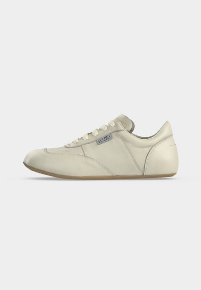 Χαμηλόδερμο sneaker σε εκρού απόχρωση με κορδόνια και μπεζ σόλα, εμφανίζεται από το πλάι σε απλό φόντο.