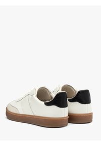 Sneakers bianche in pelle con finitura testurizzata, un accentuazione in pelle nera sul tallone e una suola in gomma marrone. Presentano un design con lacci e dettagli di cucitura.
