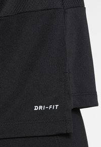 Camisa atlética negra hecha de tejido que absorbe la humedad. Presenta un dobladillo redondeado y el logo blanco de "DRI-FIT" en el lado inferior. Textura suave.