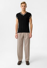 Zwart gebreid kortmouwen sweater met een V-hals, voorzien van romige boord aan de halslijn en mouwen, gecombineerd met beige broeken en bruine schoenen.