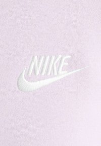 Ljus lavendeltyg med en vit broderad Nike-logotyp med swoosh. Mjuk textur och slät yta, inga synliga mönster eller detaljer.