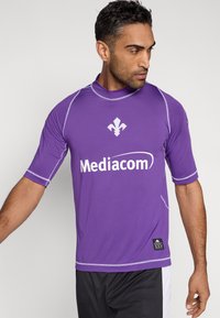 Fioletowa sportowa koszulka z krótkimi rękawami, z białym logo, zaokrąglonym dekoltem i kontrastującymi przeszyciami. Teksturowana tkanina o dopasowanym kroju.