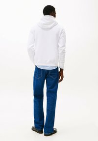 Witte capuchontrui gecombineerd met blauwe denim jeans, met een rechte pijp en twee achterzakken met gestikt detail.