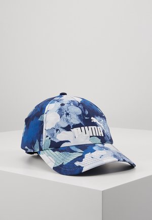 Blå og hvid Puma baseballkasket med blomsterprint, der hviler på en lysegrå overflade med hjørne.