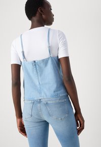 Light blue denim jumpsuit with adjustable straps, a fitted bodice, and a slightly flared bottom. Worn over a white t-shirt.