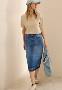 Ljust beige kortärmad stickad topp i kombination med en figurnära denim midi kjol i medelblå tvätt. Tillbehör inkluderar en denim tote och lätta sneakers.