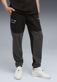 Zwarte en grijze sweatpants met een taps toelopend ontwerp, voorzien van een logo en tekst aan de zijkant. Gemaakt van gladde stof met contrasterende kleurvlakken.