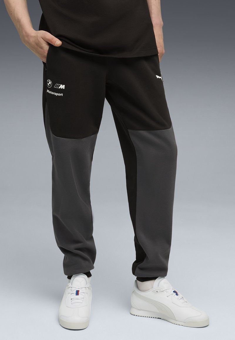 Zwarte en grijze sweatpants met een taps toelopend ontwerp, voorzien van een logo en tekst aan de zijkant. Gemaakt van gladde stof met contrasterende kleurvlakken.