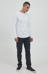 Wit katoenen overhemd met lange mouwen en ronde hals, gecombineerd met donkerblauwe broek en zwarte sneakers, met een eenvoudig, gestroomlijnd ontwerp.