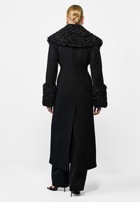 Czarny płaszcz z dużym, teksturowanym kołnierzem i mankietami. Dopasowany krój z rozcięciem z tyłu, wykonany z gładkiego materiału. Długie rękawy, elegancka sylwetka.