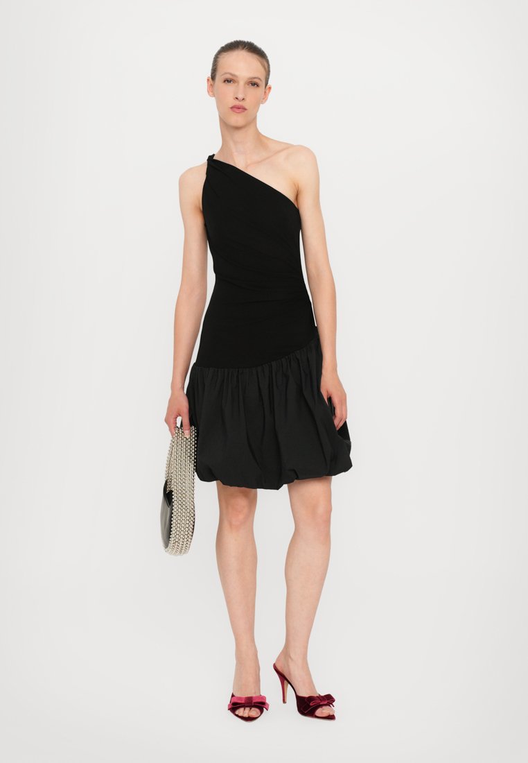 Robe noire à une épaule avec un corsage ajusté et une jupe évasée à volants. Fabriquée en tissu texturé, accompagnée d'une pochette en maille argentée et de talons en velours rouge.