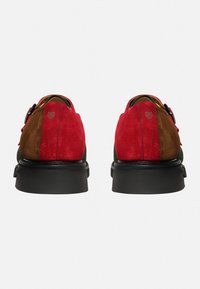 Mehrfarbige Wildlederschuhe mit roten, braunen und grünen Abschnitten, einer schwarzen Gummisohle und sichtbaren Nähdetails.