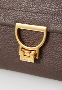 Brown textured leather bag closure with a prominent gold metal latch featuring a square design and branded detailing.