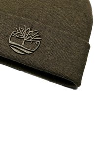 Beanie lavorato a maglia di colore verde oliva con orlo piegato, dotato di un logo ad albero testurizzato ed in rilievo sulla parte anteriore. Tessuto morbido e caldo.