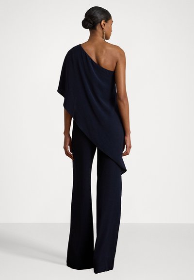 Tenue asymétrique à épaule unique en navy, avec un tissu fluide, un pantalon ample et un design original. Texture lisse, style minimaliste, sans matériel visible.