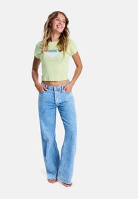 Jasnozielony krótki t-shirt z diamentowym grafiką i niebieskim tekstem, połączony z jasnoniebieskimi dżinsami z wysokim stanem o szerokich nogawkach.