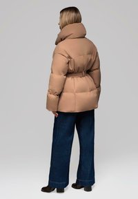 Beige puff-jakke med høj krave og bælte i taljen, parret med brede mørk denim jeans og sorte høje støvler. Glat tekstur.