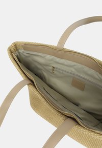 Borsa tote in paglia intrecciata beige con manici in pelle beige liscia; l'interno presenta una fodera in tessuto chiaro e una tasca con zip per lo stoccaggio.
