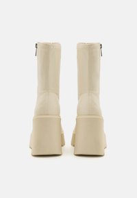 Botine bej din piele ecologică cu talpa chunky și fermoar pe spate, având o textură netedă și un design minimalist.