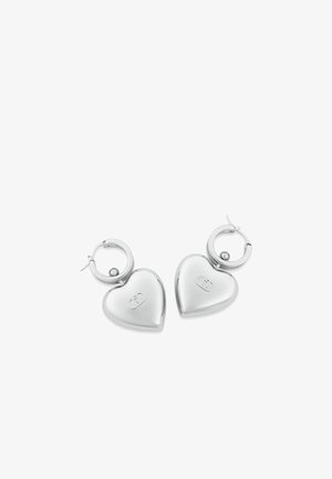 Orecchini a forma di cuore in argento con finitura lucida, attaccati a chiusure ad anello circolare. Presentano un piccolo logo sui cuori.