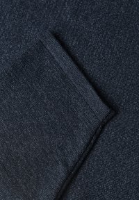 Tissu tricoté bleu foncé avec un bord plié, montrant une surface textile douce et texturée.