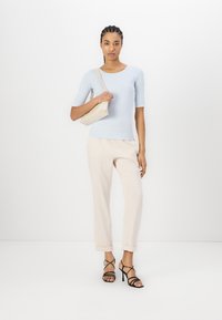Lichtblauw getailleerd shirt met korte mouwen, crème tapered broek en zwarte strappy hoge hakken, gecombineerd met een beige schoudertas.
