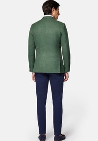 Zielona marynarka o fakturowanym materiale z klapami, z pojedynczym rozcięciem z tyłu, w połączeniu z granatowymi chinosami. Jasny kolor koszuli widoczny przy kołnierzyku.