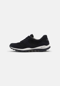 Zwarte sportieve schoen van suede en mesh materialen, met een ronde neus, veters en een dikke witte zool met een gestructureerd patroon.