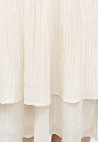 Λευκή πλισέ φούστα με στρώσεις από ελαφρύ, ημιδιάφανο ύφασμα που αφήνει να διακρίνονται τα πόδια από κάτω.