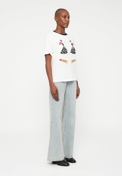 Vit bomullströja med svart kant, prydd med illustrationer av prickiga klänningar och läppstiftsdesigner. Matchad med ljusblå utsvängda jeans.