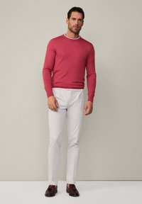 Roter Pullover mit langen Ärmeln und einem kontrastierenden weißen Kragen, kombiniert mit weißen Hosen und braunen Loafers, was einen eleganten und modernen Look schafft.