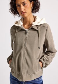Lehká khaki bomber bunda s bílou kapucí, stříbrným zipem, bočními kapsami, elastickými manžetami a hladkým povrchem.