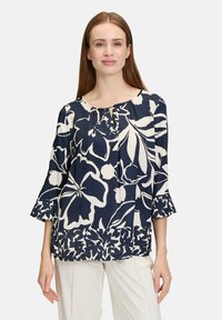 Marinebluse mit weißem Blumenmuster, runder Ausschnitt, dreiviertel Ärmel und Rüschenbündchen. Leichter Stoff mit glatter Textur.