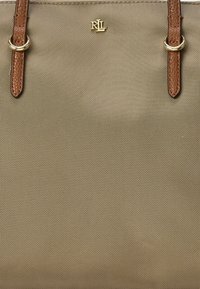 Saco tote cáqui com alças de couro castanho, hardware dourado e uma superfície texturizada. Apresenta o logo em relevo "RL" na parte da frente.