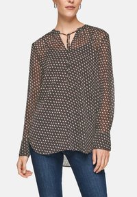 Blusa trasparente nera con un motivo di piccoli diamanti rosa, con scollo a cravatta e maniche lunghe, abbinata a jeans blu. Tessuto morbido e leggero.