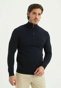 Pull-over zippé bleu marine au design ajusté avec des manches longues, des poignets et un ourlet côtelés, mettant en avant un accent zippé contrastant.