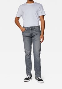 Vaqueros de denim gris con un corte ajustado, que cuentan con cinco bolsillos y un cierre de botón. Combinados con una camiseta blanca sencilla y zapatillas negras.