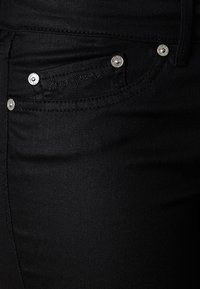 Jeans de denim negro con un bolsillo frontal decorado con remaches metálicos, textura suave y un corte ajustado.