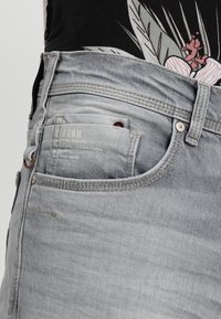 Vaqueros de mezclilla gris claro con un acabado texturizado, que cuentan con un bolsillo frontal, una sutil marca y detalles de costura en contraste.