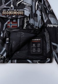 Giacca camouflage nera e grigia con logo Napapijri, rivestimento impermeabile e etichetta interna con icone di cura e caratteristiche del prodotto.