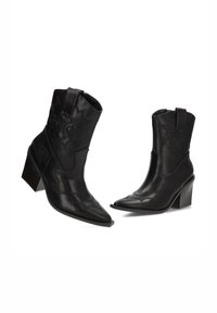 Botas de vaquero de cuero negro con punteras puntiagudas, costuras decorativas y tacón de bloque de altura media. Cuentan con cremalleras laterales y tiradores.