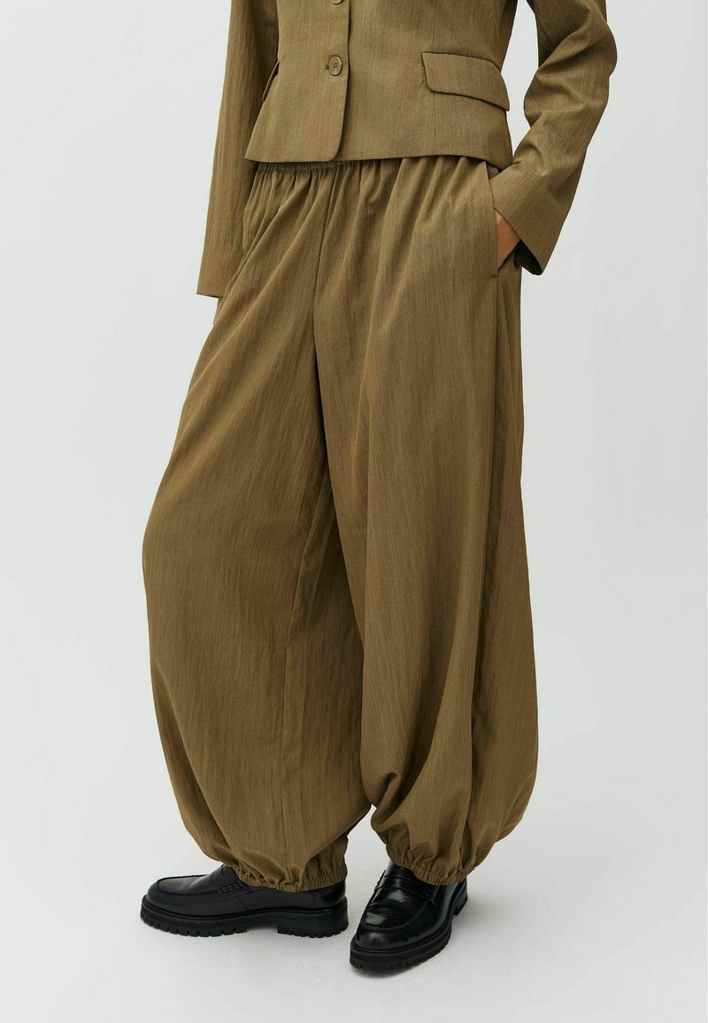 Pantalon marron ample avec poignets élastiques, assorti à une veste marron assortie et des chaussures noires épaisses sur fond blanc.