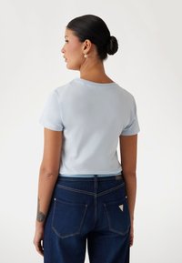 T-shirt azzurro chiaro a maniche corte con scollatura rotonda, indossato con jeans blu scuro con un logo a triangolo sulla tasca posteriore.