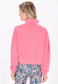 Rosa, kürz geschnittenes Sweatshirt mit hohem Kragen und langen Ärmeln, aus weichem Material, kombiniert mit bunten, gemusterten Leggings.