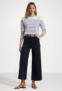 Stripet langermet skjorte i krem og blå, parret med mørke vide bukser. Outfiten er accessorert med et flettet belte og sandaler med stropper.