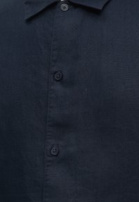 Chemise en lin bleu marine foncé avec boutons noirs et col classique, présentée à plat sans marquage visible ni motifs.