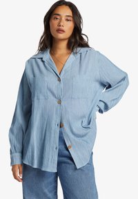 Blue and white striped button-up shirt with two front pockets and brown buttons. Relaxed fit with long sleeves and a spread collar.