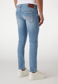 Jeans de mezclilla azul claro con un diseño ajustado, que presentan un parche de cuero en la parte posterior y dos bolsillos traseros con un logo triangular.
