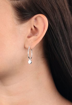 Pendientes de aro plateados con un pequeño colgante redondo. Textura suave, diseño simple y estilo de aro abierto para fácil uso.